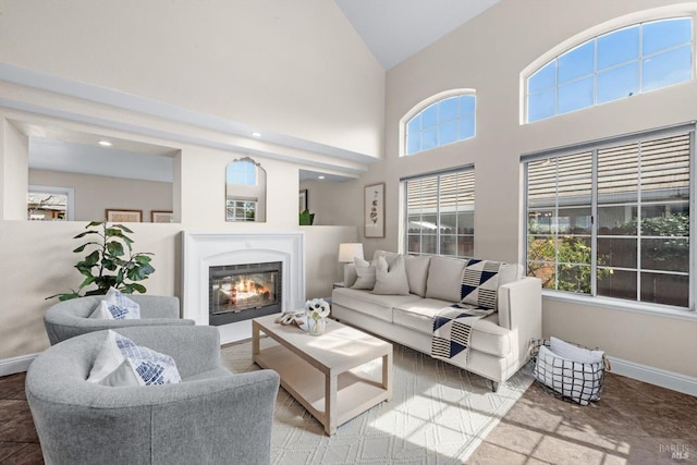 living area featuring a glass covered fireplace, high vaulted ceiling, and baseboards