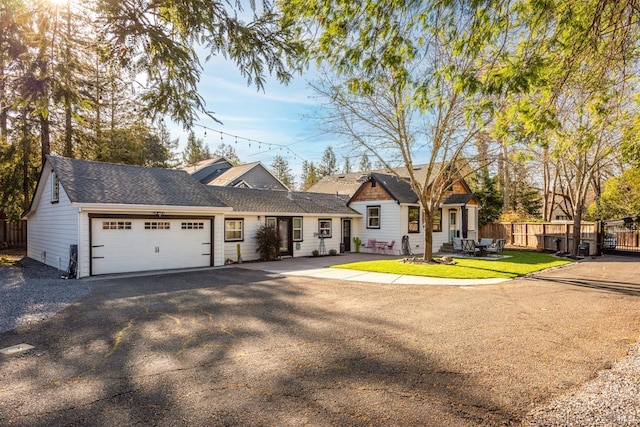 view of front of home with a front lawn, driveway, fence, a shingled roof, and a garage