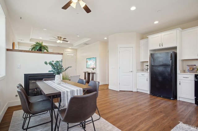 dining area with recessed lighting, a raised ceiling, wood finished floors, and a fireplace