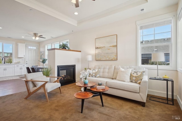 living room featuring visible vents, crown molding, recessed lighting, a glass covered fireplace, and a raised ceiling