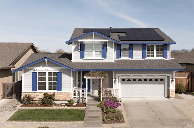 view of front of house with solar panels, fence, a porch, stone siding, and driveway