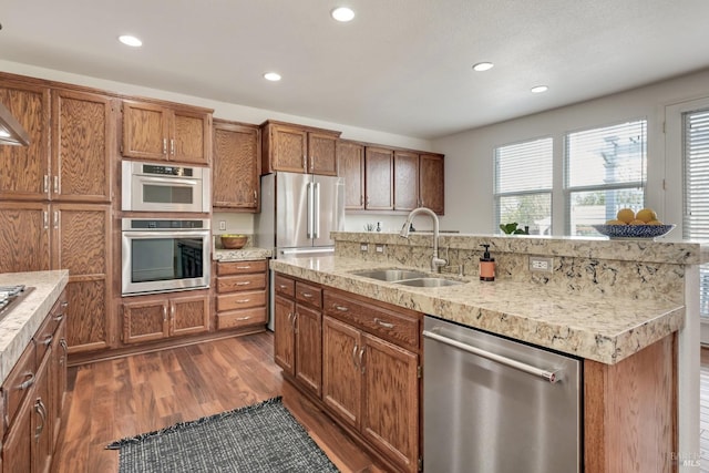 kitchen featuring brown cabinets, a sink, dark wood finished floors, recessed lighting, and appliances with stainless steel finishes