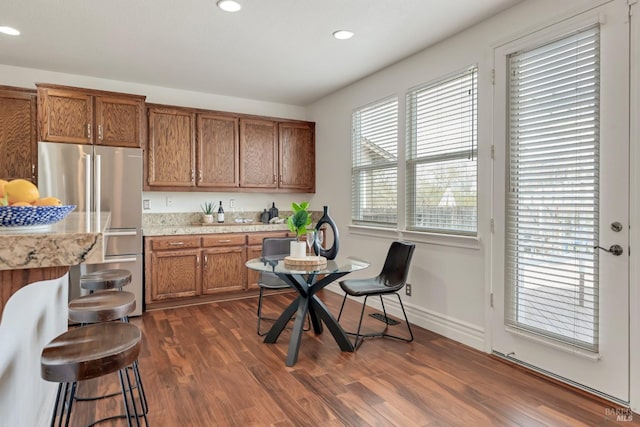 kitchen with dark wood-style floors, brown cabinetry, baseboards, recessed lighting, and freestanding refrigerator