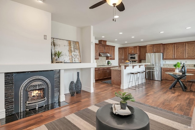 living area featuring recessed lighting, a ceiling fan, dark wood-type flooring, and a tiled fireplace