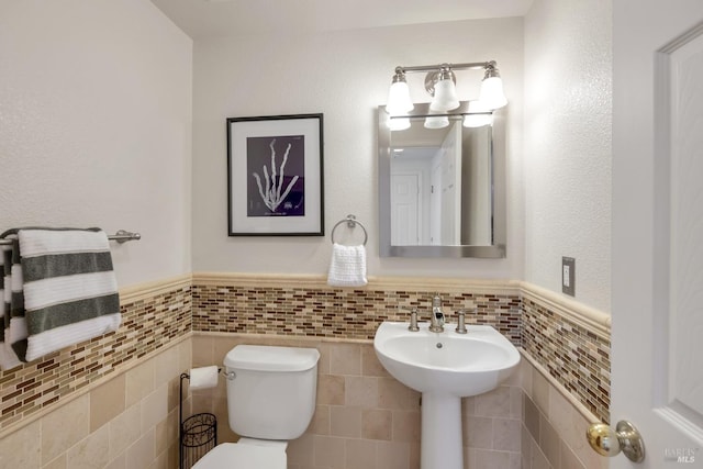 half bathroom featuring tile walls, toilet, and wainscoting