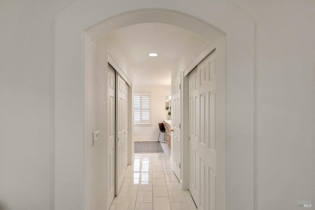 hallway featuring light tile patterned floors, baseboards, and arched walkways