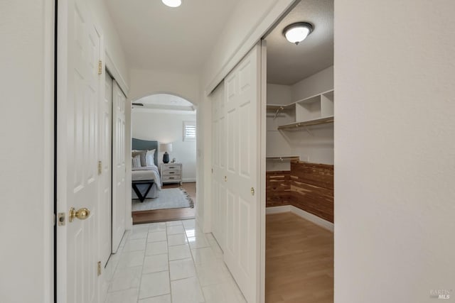 corridor featuring baseboards, arched walkways, and light wood-type flooring