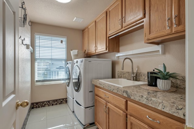 clothes washing area with visible vents, washing machine and dryer, cabinet space, a textured ceiling, and a sink