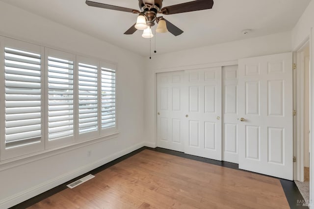 unfurnished bedroom with a ceiling fan, wood finished floors, visible vents, baseboards, and a closet