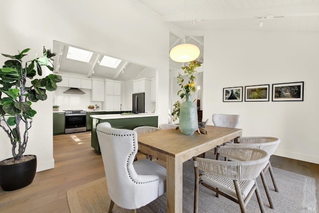 dining area with a skylight, wood finished floors, baseboards, and beam ceiling