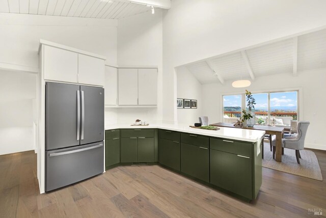 kitchen with white cabinets, green cabinetry, light countertops, freestanding refrigerator, and a peninsula