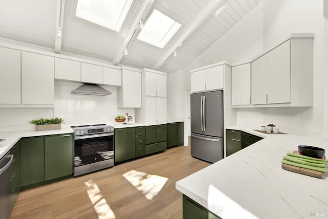 kitchen with green cabinets, wall chimney range hood, lofted ceiling with skylight, light wood finished floors, and appliances with stainless steel finishes