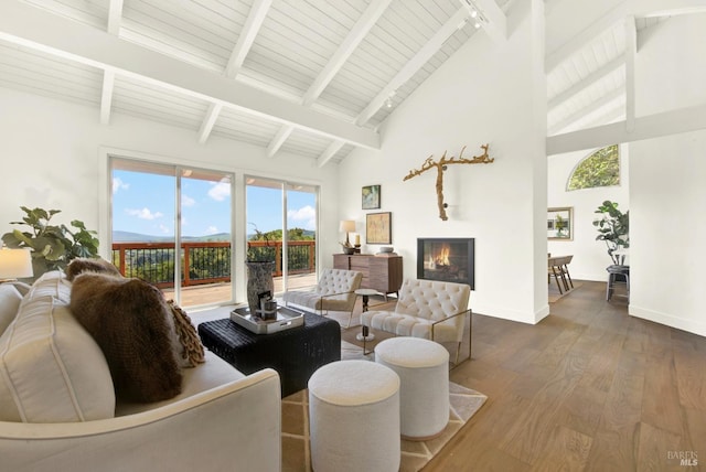 living room featuring dark wood finished floors, a glass covered fireplace, beamed ceiling, and baseboards