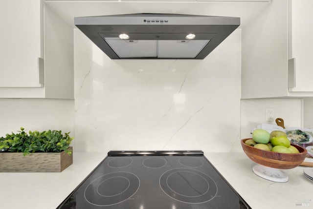 interior details featuring white cabinets, under cabinet range hood, light stone counters, and black electric cooktop