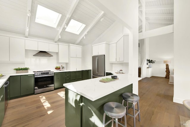 kitchen featuring wood finished floors, a skylight, under cabinet range hood, appliances with stainless steel finishes, and green cabinets