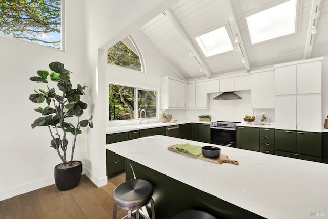 kitchen with a sink, stainless steel appliances, under cabinet range hood, a kitchen bar, and beamed ceiling