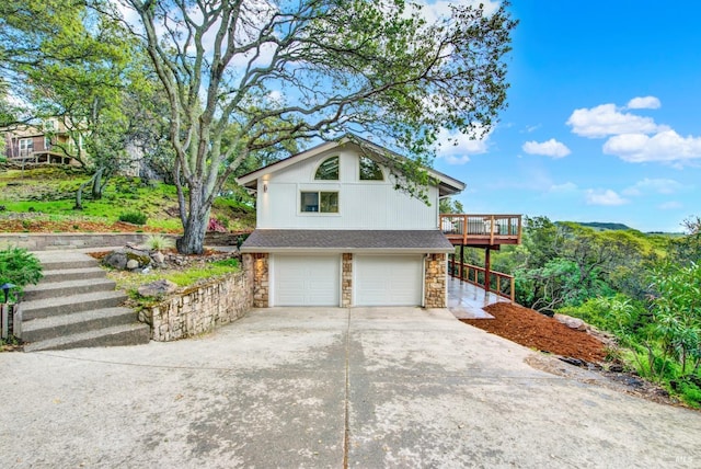 view of home's exterior featuring stone siding, driveway, an attached garage, and stairs