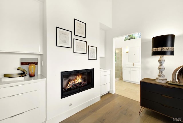 interior space featuring connected bathroom, baseboards, a warm lit fireplace, a high ceiling, and wood finished floors