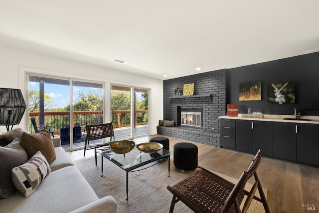 living room featuring visible vents, a brick fireplace, wet bar, recessed lighting, and wood finished floors