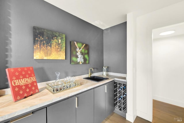 bar featuring wood finished floors, wet bar, a sink, and baseboards
