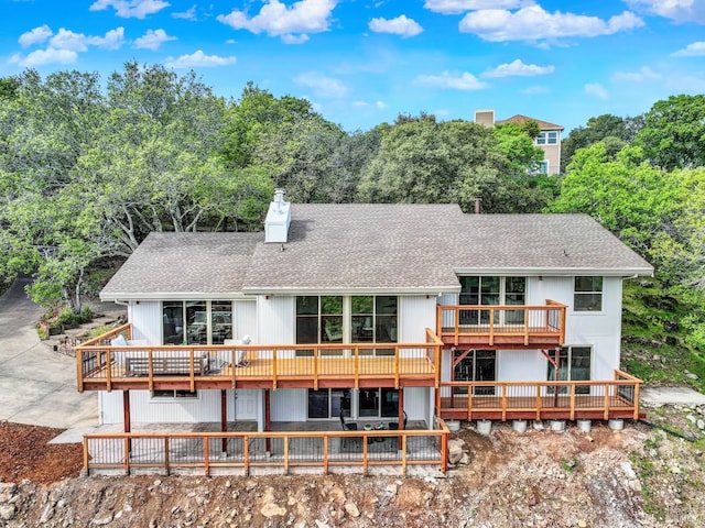 back of property with a wooden deck, a chimney, and a shingled roof