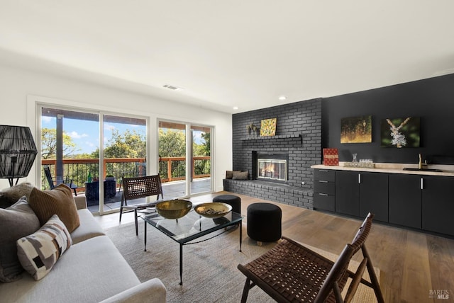 living area with visible vents, a brick fireplace, indoor wet bar, recessed lighting, and wood finished floors