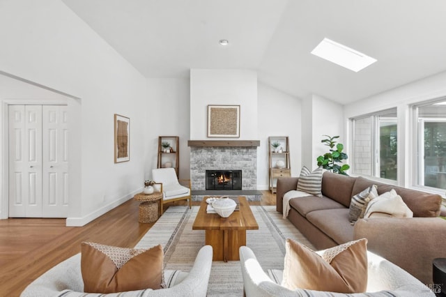 living area featuring baseboards, high vaulted ceiling, a skylight, a fireplace, and light wood-type flooring