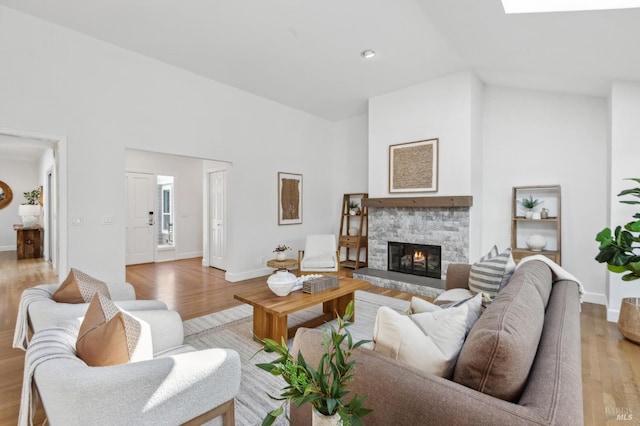 living room featuring baseboards, high vaulted ceiling, light wood-style flooring, and a fireplace