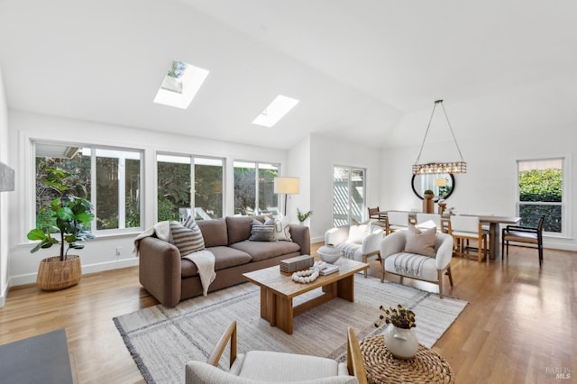 living area with vaulted ceiling with skylight, baseboards, and light wood-type flooring