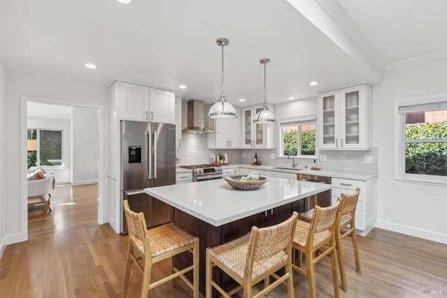 kitchen featuring a sink, appliances with stainless steel finishes, a breakfast bar area, and wall chimney range hood