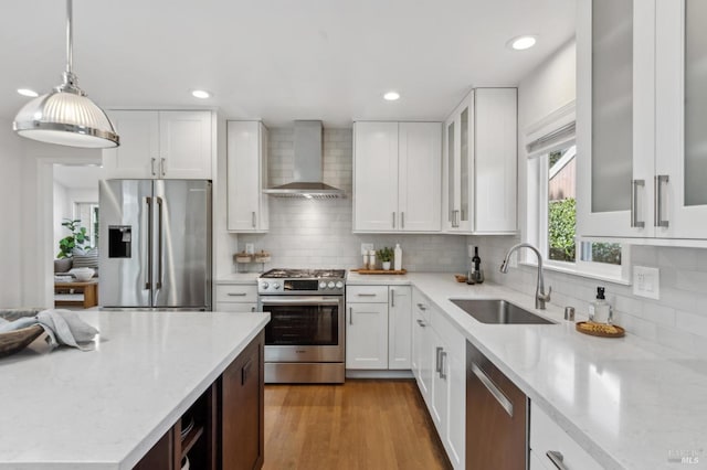 kitchen featuring white cabinets, stainless steel appliances, wall chimney range hood, and a sink