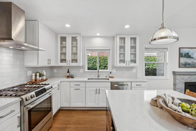 kitchen featuring white cabinets, appliances with stainless steel finishes, wall chimney exhaust hood, and a sink