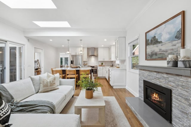 living area with light wood-type flooring, ornamental molding, recessed lighting, a skylight, and a fireplace