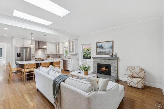 living room featuring a fireplace, crown molding, baseboards, and light wood-type flooring