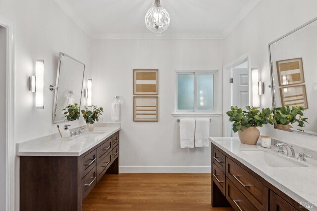 full bath with a sink, two vanities, wood finished floors, and ornamental molding