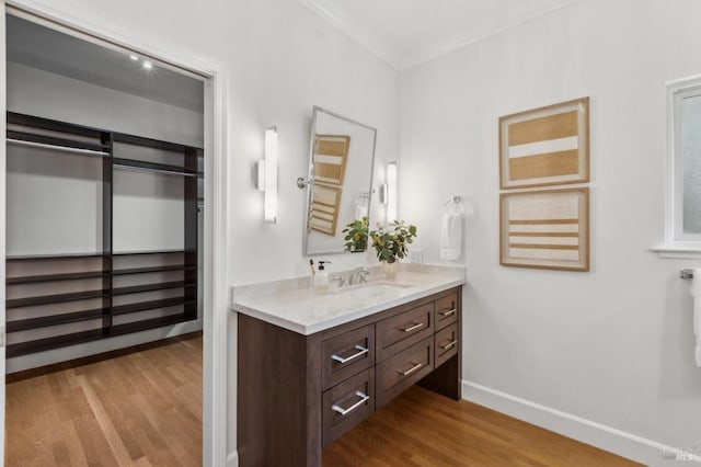 bathroom featuring baseboards, wood finished floors, vanity, and ornamental molding