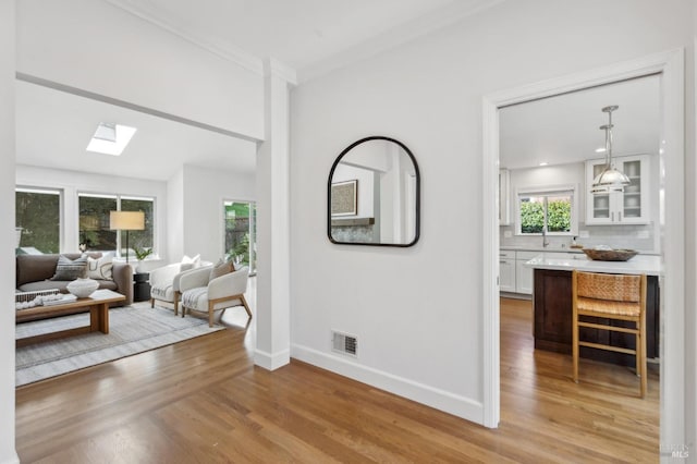 hall featuring visible vents, light wood-style flooring, a skylight, crown molding, and baseboards