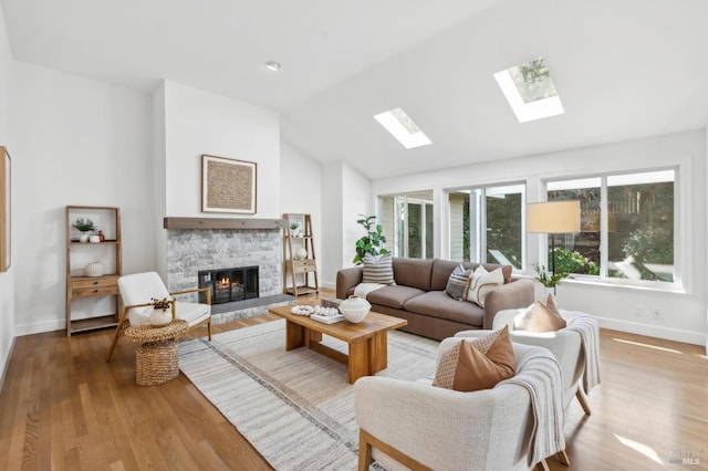 living area featuring wood finished floors, vaulted ceiling with skylight, a fireplace, and baseboards