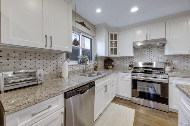 kitchen featuring light wood-type flooring, under cabinet range hood, a sink, stainless steel appliances, and white cabinets