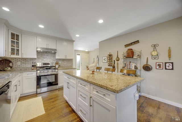 kitchen featuring backsplash, under cabinet range hood, dishwashing machine, light wood-style floors, and stainless steel gas range