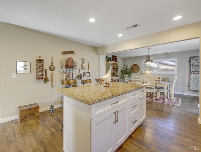 kitchen with visible vents, a center island, dark wood-type flooring, light stone countertops, and white cabinets