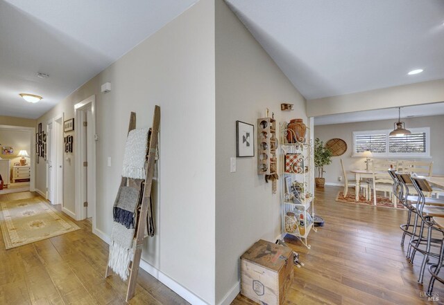 hallway featuring vaulted ceiling, baseboards, and hardwood / wood-style floors