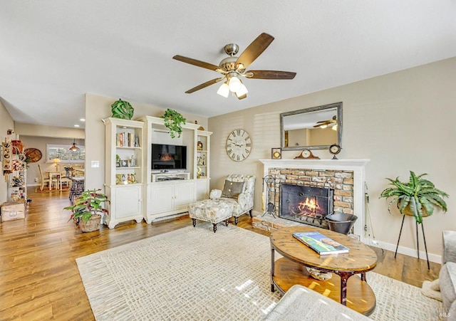 living room with a warm lit fireplace, baseboards, ceiling fan, and wood finished floors