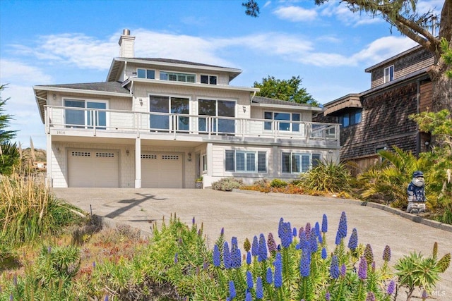 view of front of home featuring a chimney, driveway, an attached garage, and a balcony