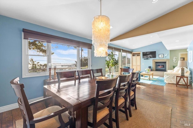 dining area featuring a glass covered fireplace, wood-type flooring, baseboards, and vaulted ceiling