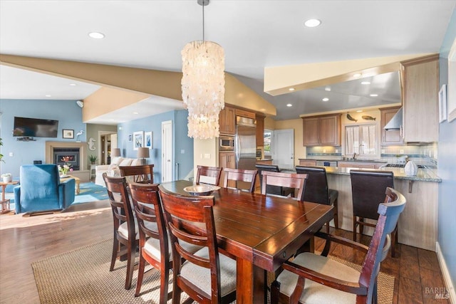 dining room with a notable chandelier, recessed lighting, a lit fireplace, dark wood-style flooring, and vaulted ceiling