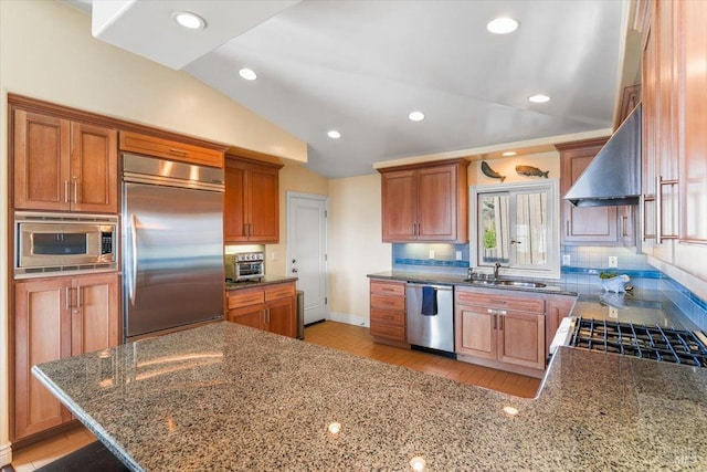 kitchen with wall chimney range hood, built in appliances, lofted ceiling, decorative backsplash, and stone countertops