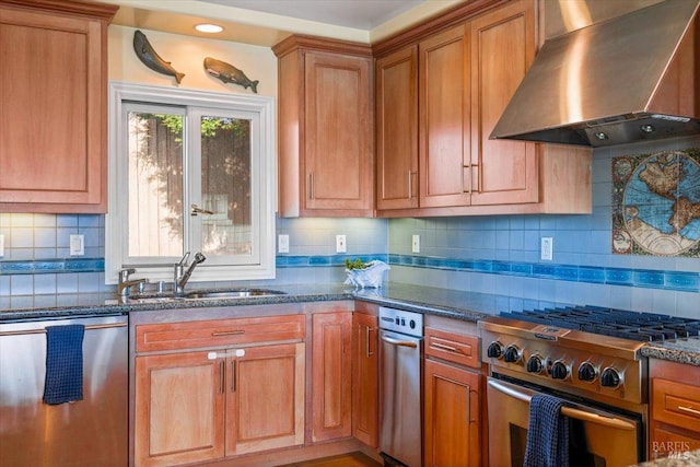 kitchen with dark stone countertops, wall chimney range hood, appliances with stainless steel finishes, and a sink