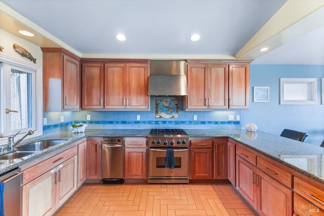 kitchen with dark stone counters, recessed lighting, a sink, stainless steel appliances, and wall chimney exhaust hood