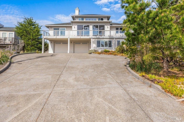 view of front facade with a garage, a balcony, a chimney, and driveway